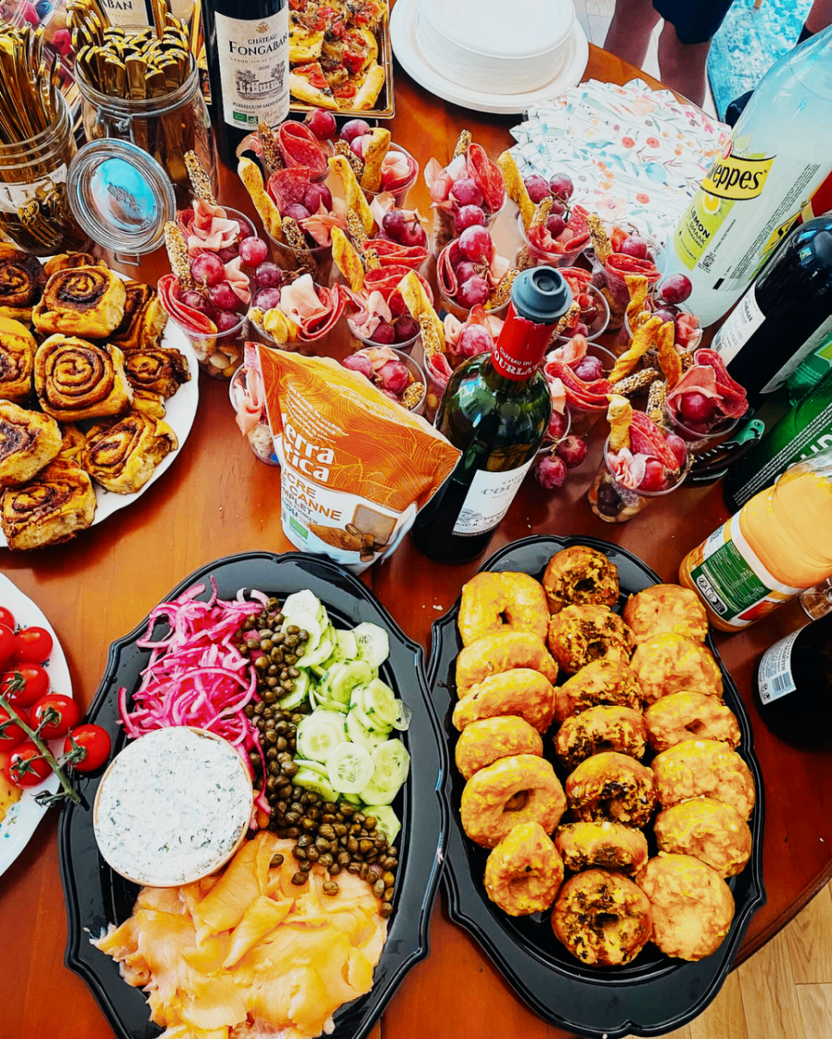Charcuterie-style spread with bagels, dips, pastries, and drinks for a gathering