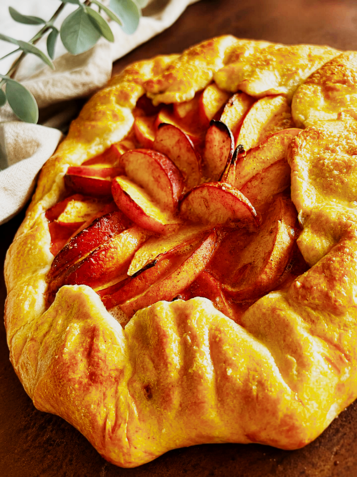 Golden peach galette styled with eucalyptus on a warm tabletop